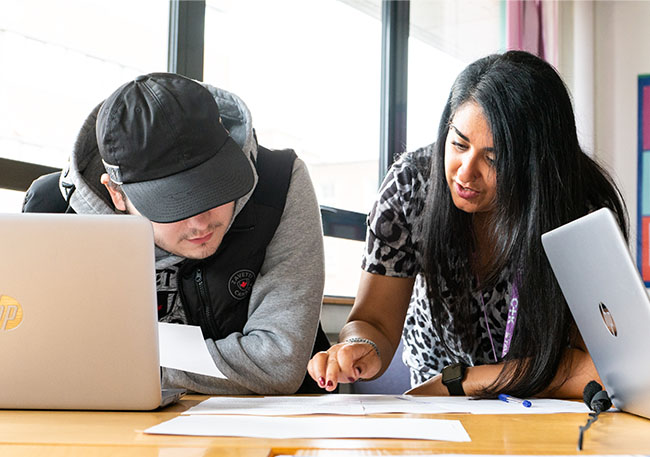 Careers adviser engaging with a client looking at paperwork and a laptop on desk in a careers office